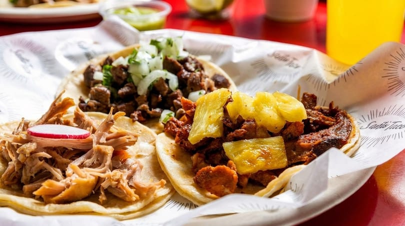 Three Santo Taco street tacos with various fillings, including pork, beef, and pineapple.