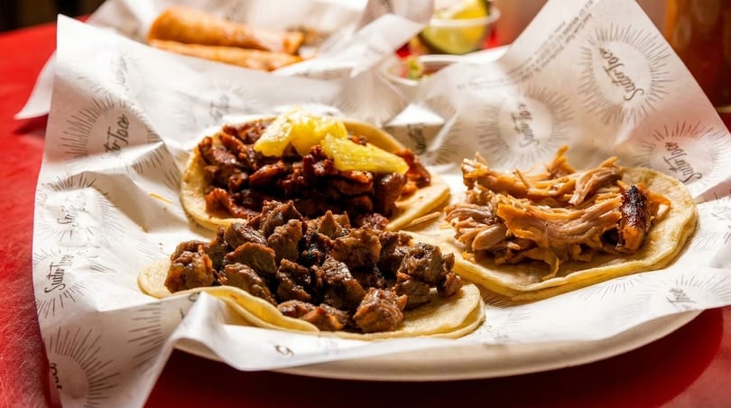 Three delicious tacos with various meat fillings and pineapple on branded paper.